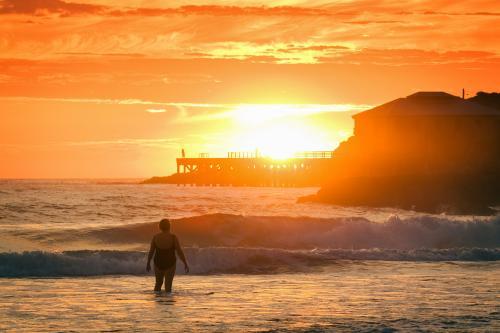 A woman at the beach at sunrise, wharf in the background. - Australian Stock Image