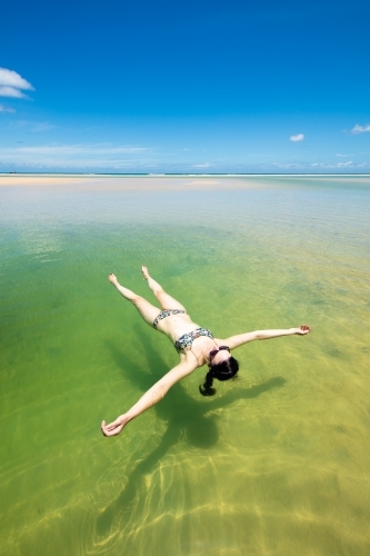 A woman floats in a pool of seawater by the sunny beach on Moreton Island - Australian Stock Image