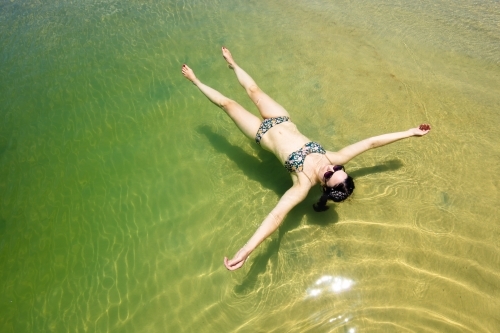 A woman floats in a pool of seawater by the sunny beach on Moreton Island - Australian Stock Image