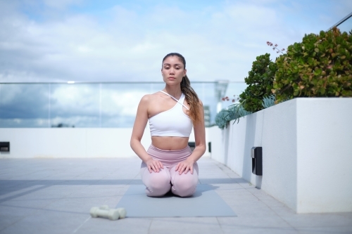 A woman in a white tank top and pink leggings working out using white dumbbells - Australian Stock Image