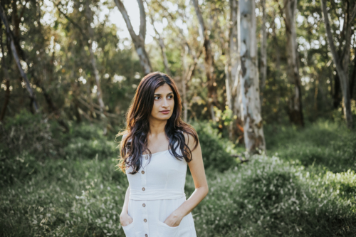 a woman standing amidst a sunlit park forest - Australian Stock Image
