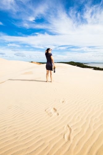 A woman stands high on a sand dune viewing into the distance of Moreton Bay. - Australian Stock Image