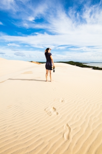 A woman stands high on a sand dune viewing into the distance of Moreton Bay.