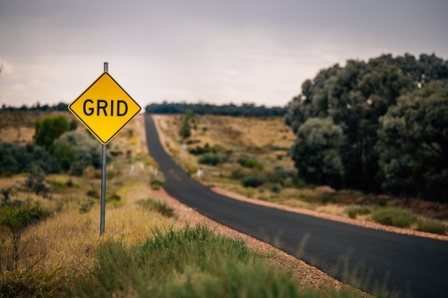 A yellow diamond-shaped road sign with the word “GRID” placed on the left side of a two-lane road - Australian Stock Image