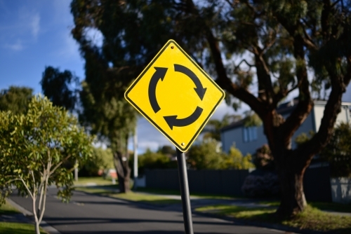A yellow roundabout street sign bathed in sunlight