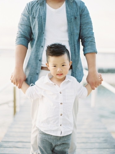 A young boy holding hands with his father walking a long a wharf - Australian Stock Image