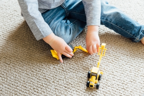 A young boy playing with a small yellow toy digger