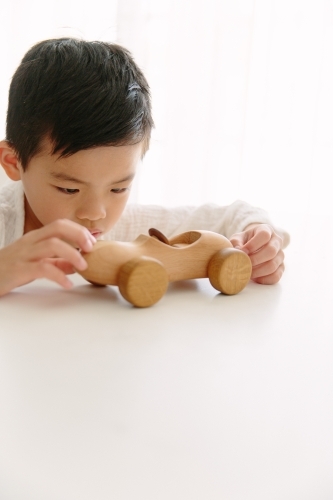 A young boy playing with his wooden car at home sitting at the table - Australian Stock Image