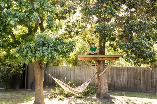 A young boy sitting in a tree house and a girl lying in a hammock in an australian backyard - Australian Stock Image