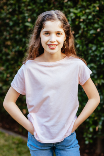 A young caucasian girl poses in front of a green hedge on a sunny evening in Australia - Australian Stock Image