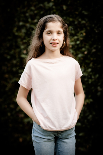 A young caucasian girl poses in front of a green hedge on a sunny evening in Australia - Australian Stock Image