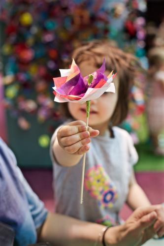 A young girl / child holds up a paper flower she has made