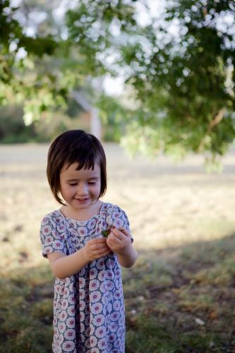 A young girl / child playing under a tree in a park at sunset - Australian Stock Image