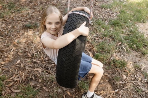 A young girl sitting on a home made tyre swing playground - Australian Stock Image