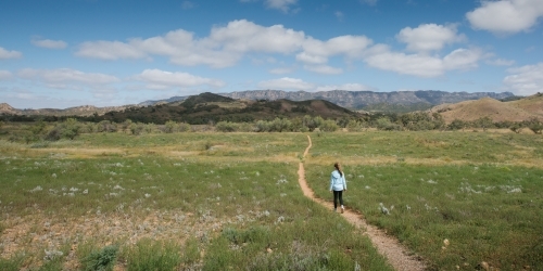 A young girl walking down a single bush trail towards a mountain range