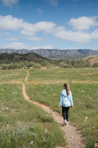 A young girl walking down a single bush trail towards a mountain range - Australian Stock Image
