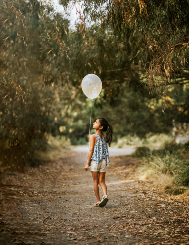 A young girl walking holding a white balloon - Australian Stock Image