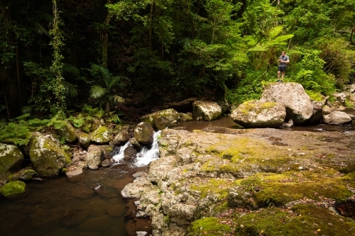 A young male standing atop a large boulder in the middle of a small stream. - Australian Stock Image