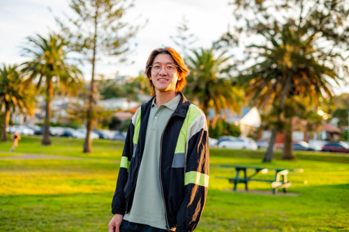 A young man stands smiling under palm trees in a vibrant park during golden hour. - Australian Stock Image