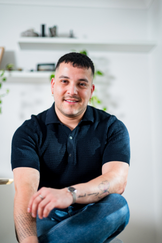 A young man with short hair sits comfortably, looking cheerful in stylish clothes. - Australian Stock Image