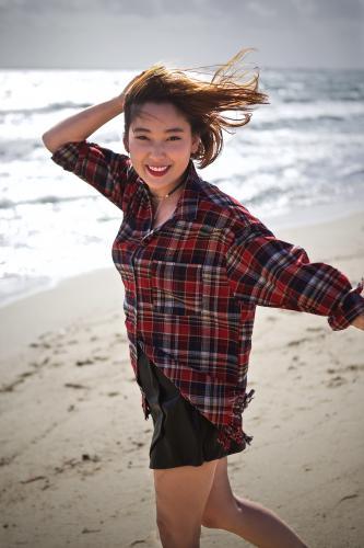 A young woman enjoying the sun on the beach by the water - Australian Stock Image