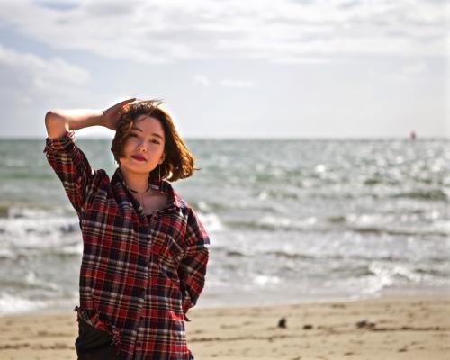 A young woman enjoying the sun on the beach by the water - Australian Stock Image