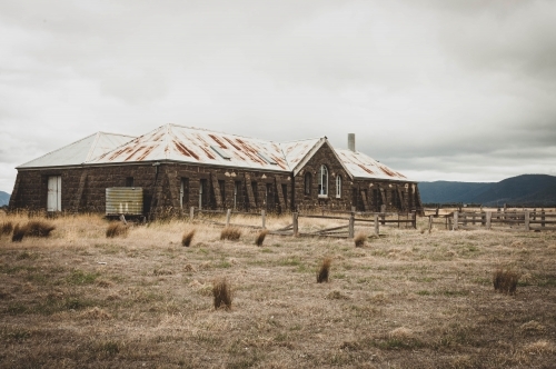 abandoned bluestone shearing shed in the dry grassy landscape - Australian Stock Image