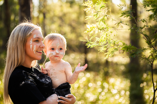 Aboriginal Australian mum and baby with feeding tube enjoying natural bushland painted with ochre - Australian Stock Image