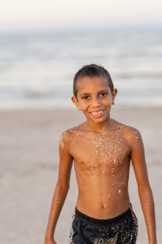 aboriginal boy on beach with sand stuck to him from where he has been playing - Australian Stock Image