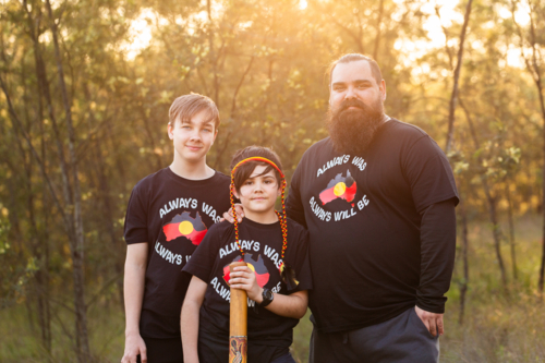 Aboriginal dad standing together with boys in golden light in Australian bushland - Australian Stock Image
