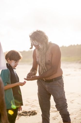 Aboriginal father with body paint helping his son on a beach