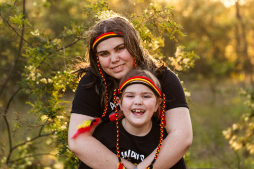 Aboriginal girl and big sister with red yellow and black headband in Australian bushland - Australian Stock Image