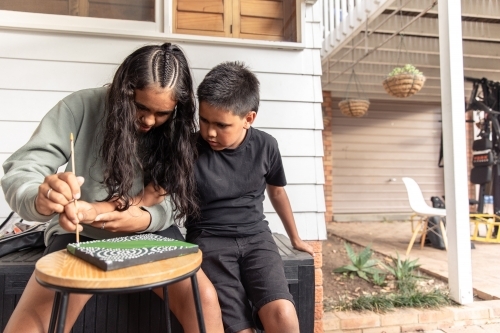 Aboriginal girl and boy dot painting together - Australian Stock Image