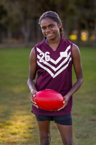 aboriginal girl smiling and holding a red leather football - Australian Stock Image