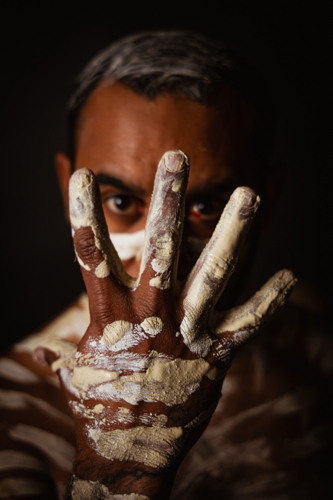 Aboriginal male holding up painted hand over face - Australian Stock Image