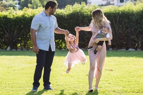 Aboriginal man Caucasian woman with children swinging daughter - Australian Stock Image