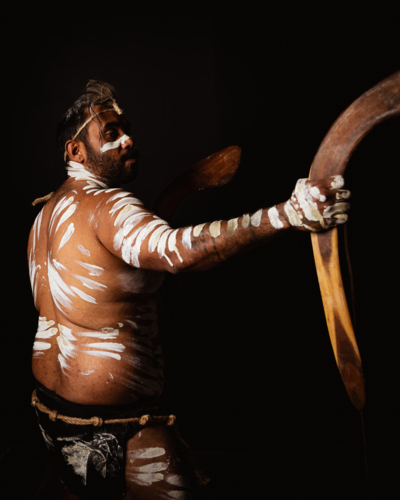 Aboriginal man holding a pair of boomerangs in a dark background. - Australian Stock Image