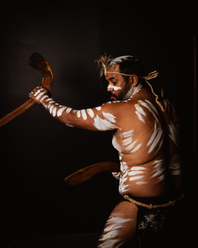 Aboriginal man holding a pair of boomerangs in a dark background. - Australian Stock Image