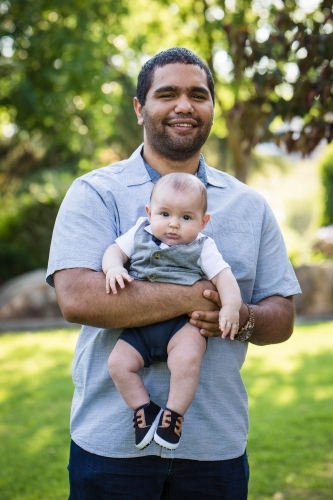 Aboriginal man smiling holding baby - Australian Stock Image