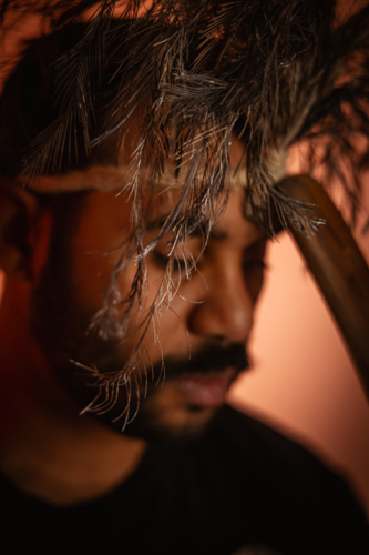 Aboriginal man wearing feathered headdress holding wooden boomerang close to his forehead - Australian Stock Image