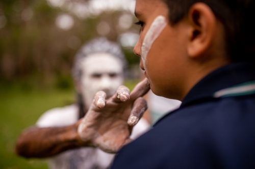 Aboriginal man wearing white face paint putting white face paint onto a young Aboriginal boy