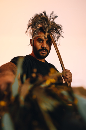 Aboriginal man with head piece pointing gum leaves to foreground - Australian Stock Image