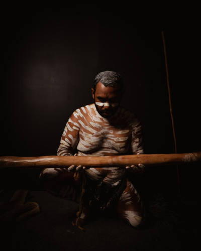 Aboriginal man with white body paint holding a wooden didgeridoo. - Australian Stock Image