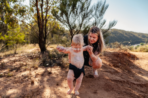 Aboriginal mum with her baby boy together by cliff on country in Australian bushland - Australian Stock Image