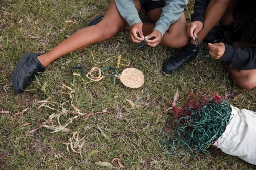 Aboriginal people sitting on grass, basket weaving together - Australian Stock Image