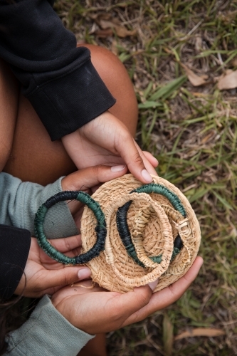 Aboriginal people sitting on grass, weaving fibre baskets and bracelets - Australian Stock Image