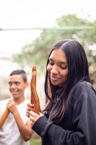 Aboriginal teenage girl with musical sticks in her backyard  with her brother - Australian Stock Image