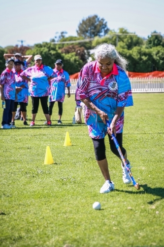 Aboriginal woman running with hockey stick and ball around safety cones - Australian Stock Image