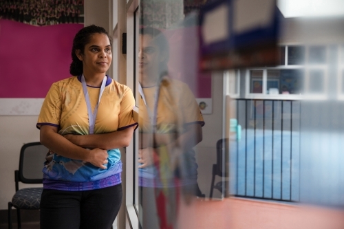 Aboriginal woman wearing lanyard looking out window - Australian Stock Image