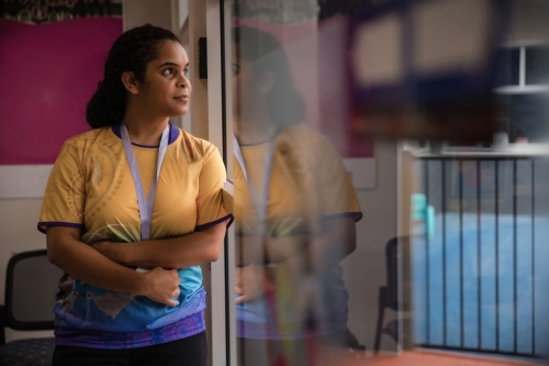 Aboriginal woman wearing lanyard looking out window - Australian Stock Image